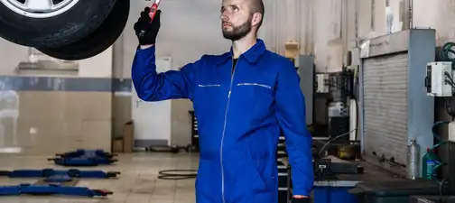 Liftteki aracın altında çalışan mavi tulumlu oto servis çalışanı